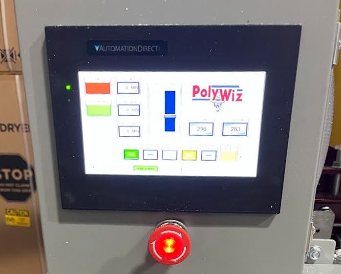 A touchscreen control panel labeled "PolyWiz" displays various buttons, numbers, and indicators. Below the screen is a large illuminated red emergency stop button. Cardboard boxes and styrofoam recycling equipment are visible in the background.